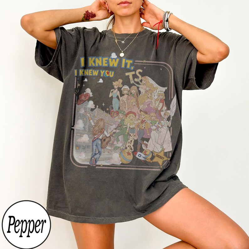 May include: A charcoal gray short-sleeve t-shirt featuring a graphic print of various animated characters and the text I KNEW IT, I KNEW YOU TS. The design includes a central figure playing a guitar, surrounded by multiple characters, a star, and a ball.