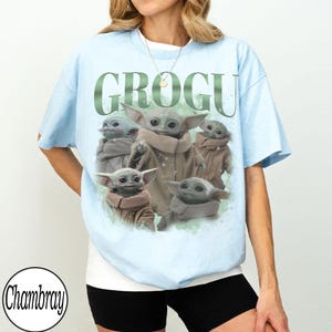 Puede incluir: Camiseta azul claro con un gr&aacute;fico de Grogu, tambi&eacute;n conocido como Baby Yoda, y la palabra "GROGU" en verde. El gr&aacute;fico muestra a Grogu en varias poses. La camiseta tiene mangas cortas.