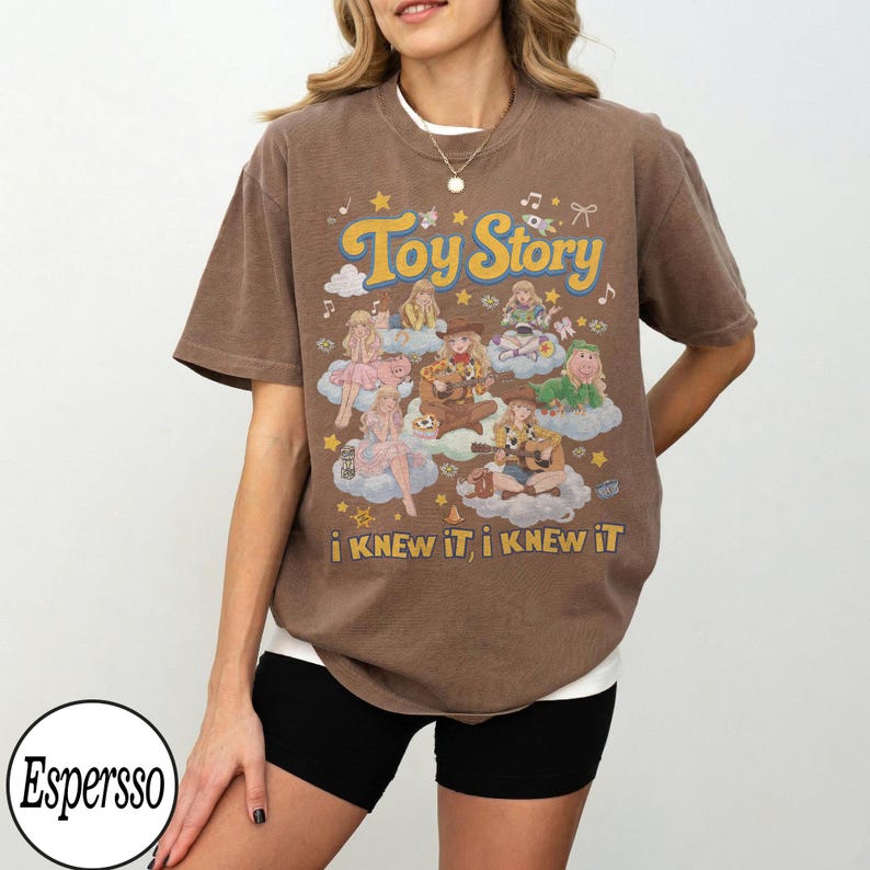 Może przedstawiać: Brązowy t-shirt z kr&oacute;tkim rękawem z nadrukiem graficznym zawierającym tekst Toy Story oraz i KNEW iT, i KNEW iT. Wz&oacute;r przedstawia wiele ilustrowanych postaci siedzących na chmurach, otoczonych małymi gwiazdkami, nutami i kokardkami.