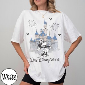 May include: White t-shirt with a graphic of Minnie Mouse in front of a castle with fireworks and the text "Walt Disney World". The design is in shades of blue, grey, and black.