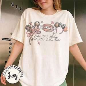 Puede incluir: Camiseta color crema con un dise&ntilde;o de Tow Mater, un lazo rosa y el texto "Like Tuh-Mater But without the Tuh." La camiseta tambi&eacute;n tiene un logotipo de Comfort Colors.