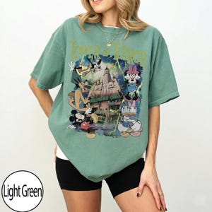 K&ouml;nnte beinhalten: Hellgr&uuml;nes T-Shirt mit einem Aufdruck des Hollywood Tower Hotels, Mickey Mouse, Minnie Mouse, Donald Duck und Goofy. Der Text "Tower of Terror" befindet sich &uuml;ber dem Aufdruck. Das Shirt hat eine lockere Passform.