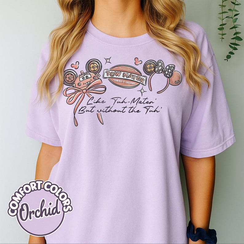 Puede incluir: Camiseta color orqu&iacute;dea con un dise&ntilde;o de Tow Mater de la pel&iacute;cula Cars, con el texto "Like Tuh-Maten' But without the Tuh." El dise&ntilde;o incluye elementos de dibujos animados y un lazo. La camiseta es de Comfort Colors.