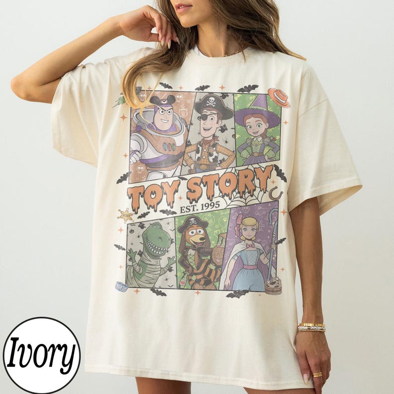 May include: An ivory short-sleeve t-shirt featuring a graphic print of Toy Story characters in Halloween costumes. The design includes Buzz Lightyear, Woody, Jessie, Rex, Slinky Dog, and Bo Peep, with the text "TOY STORY EST. 1995" and bats.