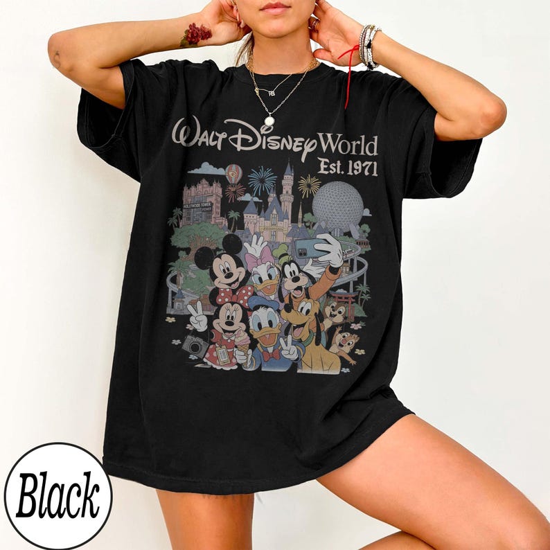 May include: A black short-sleeve t-shirt featuring a graphic print of Walt Disney World Est. 1971. The design includes illustrations of Mickey Mouse, Minnie Mouse, Donald Duck, Daisy Duck, Goofy, Pluto, and Chip 'n Dale in front of park landmarks.