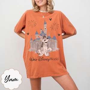 May include: Orange t-shirt with a graphic of Pluto and Cinderella's castle at Walt Disney World. The design includes fireworks and Mickey Mouse silhouettes. The text "Walt Disney World" is printed below the castle.