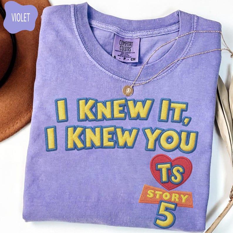 Puede incluir: Una camiseta violeta de manga corta con el texto bordado "I KNEW IT, I KNEW YOU" en amarillo con bordes azules. Debajo del texto hay un coraz&oacute;n rojo que contiene las letras "TS" y el texto "STORY 5" en amarillo con bordes azules.