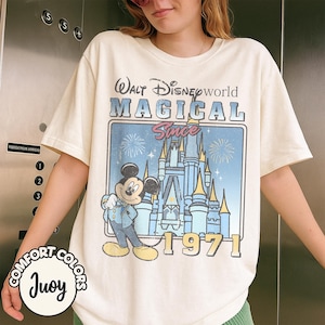 May include: Cream-colored t-shirt featuring a graphic of Mickey Mouse in front of Cinderella's castle, with the text "Walt Disney World MAGICAL Since 1971." The shirt has a vintage look and the brand name "Comfort Colors" is visible.