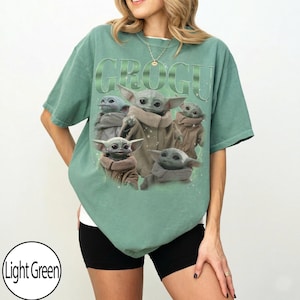 Puede incluir: Camiseta verde claro con la palabra "GROGU" en una fuente verde claro texturizada. La camiseta muestra un gr&aacute;fico de Grogu, tambi&eacute;n conocido como Baby Yoda, en varias poses. La camiseta es de corte holgado.