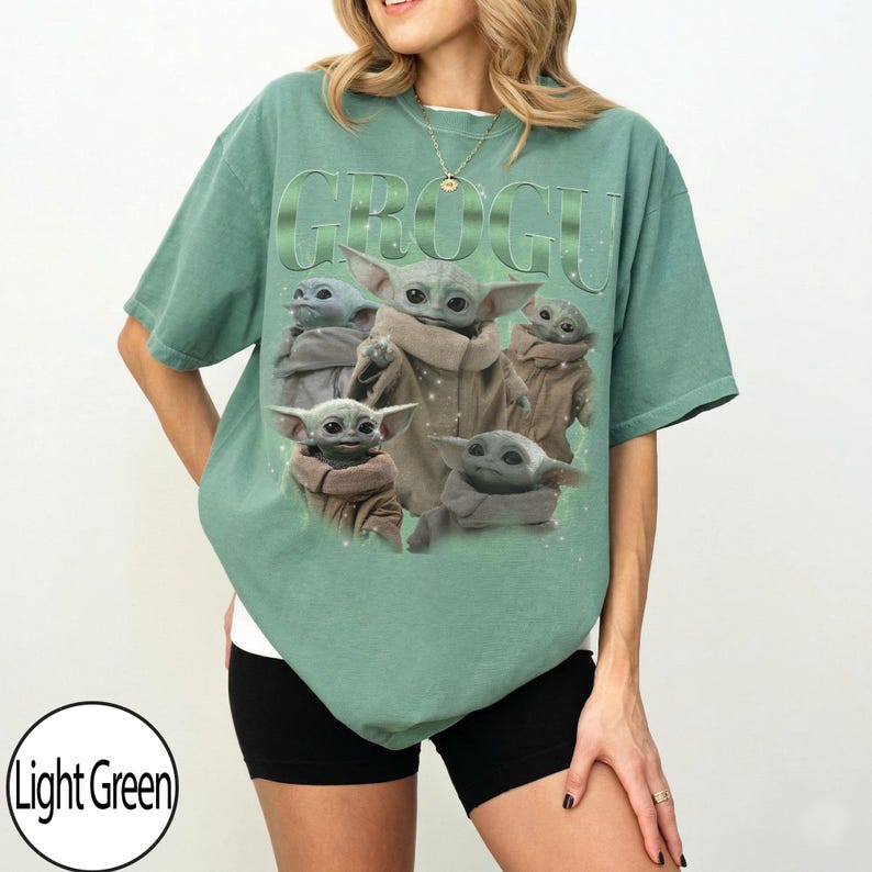 Puede incluir: Camiseta verde claro con la palabra "GROGU" en una fuente verde claro texturizada. La camiseta muestra un gr&aacute;fico de Grogu, tambi&eacute;n conocido como Baby Yoda, en varias poses. La camiseta es de corte holgado.