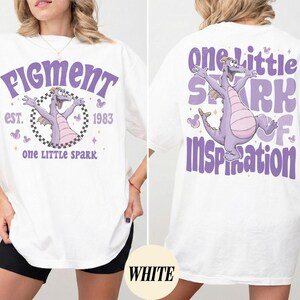 May include: White t-shirt featuring a purple dragon graphic with the text "Figment" and "One Little Spark" on the front. The back of the shirt has a matching design with the words "One Little Spark of Inspiration".