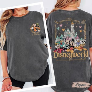 May include: Dark gray t-shirt featuring a Disney theme. The front has a small graphic of Goofy with the text "Custom Name". The back displays a larger design with Disney characters, a castle, and the text "Disneyworld - 1971".