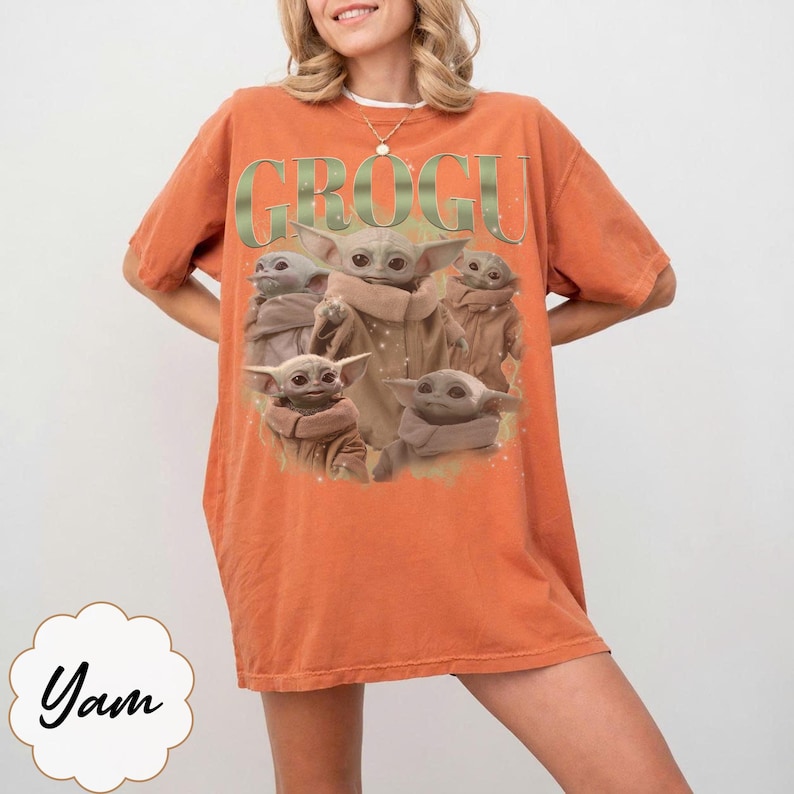 Puede incluir: Camiseta naranja con un gr&aacute;fico de Grogu, tambi&eacute;n conocido como Baby Yoda, y la palabra "GROGU" en letras verdes. La imagen muestra a Grogu en varias poses. La camiseta es de corte holgado.