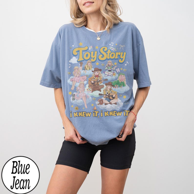Może przedstawiać: Niebieska koszulka z kr&oacute;tkim rękawem z nadrukiem graficznym zawierającym tekst Toy Story oraz i KNEW IT, i KNEW IT. Wz&oacute;r przedstawia wiele ilustrowanych postaci siedzących na chmurach, otoczonych małymi gwiazdkami, nutami i kokardkami.
