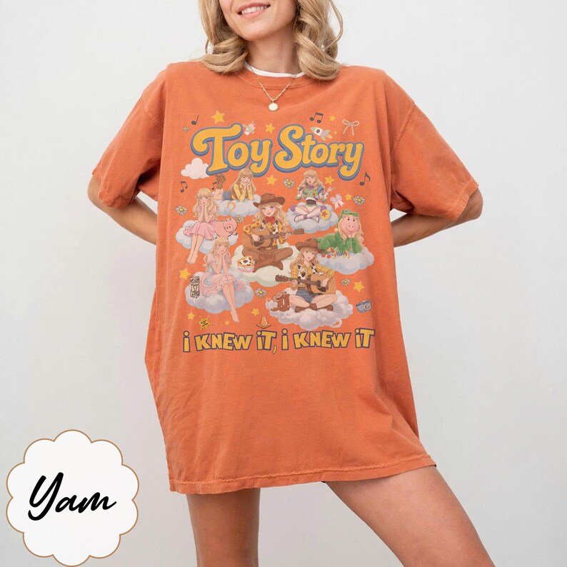 Może przedstawiać: Pomarańczowy t-shirt z kr&oacute;tkim rękawem z nadrukiem graficznym zawierającym tekst "Toy Story" oraz "i KNEW iT, i KNEW iT". Wz&oacute;r przedstawia wiele ilustrowanych postaci siedzących na chmurach, otoczonych małymi gwiazdkami, nutami i kokardkami.