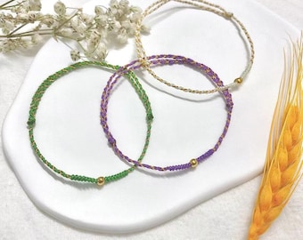 Könnte beinhalten: Drei Freundschaftsarmbänder mit goldenen Perlen. Die Armbänder sind grün, lila und weiß.
