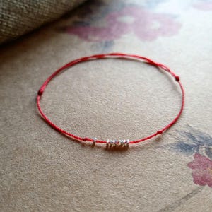 May include: A red string bracelet with silver beads that spell out the word "LOVE".
