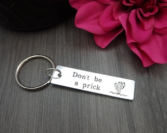 May include: Silver keychain with a rectangular tag that reads "Don't be a prick" with a small cactus illustration.