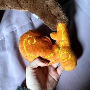 May include: A brown plush toy with a curled tail and a smaller orange plush toy with a yellow swirl design.