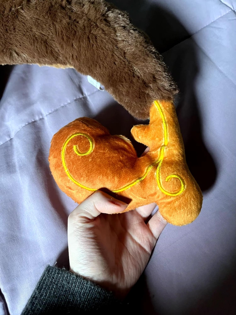 May include: A brown plush toy with a curled tail and a smaller orange plush toy with a yellow swirl design.