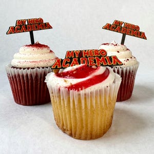 May include: Three cupcakes decorated with red and white frosting and topped with "My Hero Academia" themed toppers.
