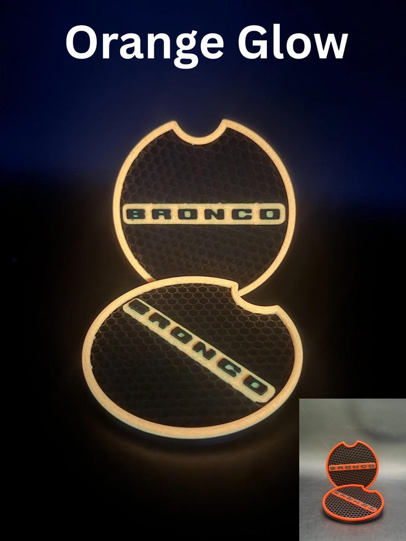 Puede incluir: Dos insertos circulares para portavasos de coche con una textura de panal negra y la palabra BRONCO en letras naranjas. Los bordes de los insertos brillan con una luz naranja, y el texto Orange Glow aparece en la parte superior.