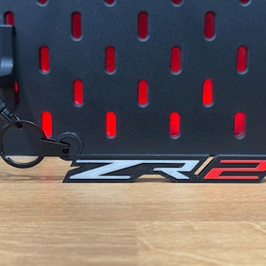 May include: Black keychain with a silver and red "ZR2" logo. The keychain has a metal ring for attaching to keys.