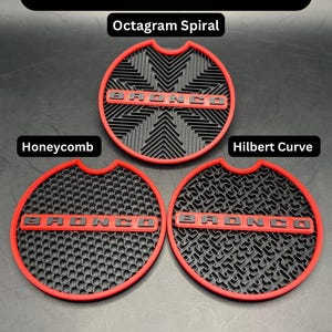 Puede incluir: Tres insertos circulares rojos y negros para portavasos con el texto BRONCO en relieve en cada uno. Los patrones incluyen Octagram Spiral, Honeycomb y Hilbert Curve. El texto Non-Glow Red y Base Patterns es visible en el fondo negro.