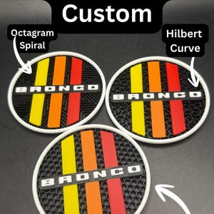 Puede incluir: Tres emblemas circulares personalizados con borde blanco, cada uno con la palabra BRONCO en letras blancas sobre tres franjas verticales en amarillo, naranja y rojo. Los patrones de fondo incluyen una espiral de octagrama, una curva de Hilbert y un panal.