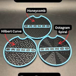 Puede incluir: Tres insertos circulares para portavasos de coche con borde exterior azul claro y base negra. Cada inserto presenta el texto BRONCO en relieve. Los patrones est&aacute;n etiquetados como Honeycomb, Hilbert Curve y Octagram Spiral. Texto Blue Glow.