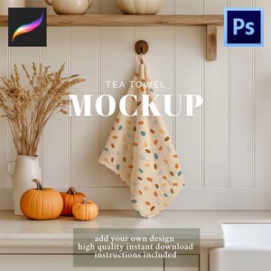 Op de afbeelding: Een theedoek-mockup met een beige achtergrond en een patroon van kleurrijke ovalen. De handdoek hangt aan een houten haak. Het woord "MOCKUP" wordt in grote witte letters weergegeven. Pompoenen en een vaas met tarwe staan op de voorgrond.