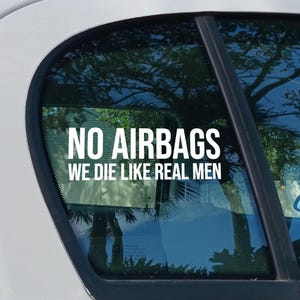 Puede incluir: Calcomanía de vinilo blanco aplicada a una ventana de coche. El texto "NO AIRBAGS WE DIE LIKE REAL MEN" está escrito en negrita, con una fuente sans-serif. La ventana del coche refleja árboles y cielo.