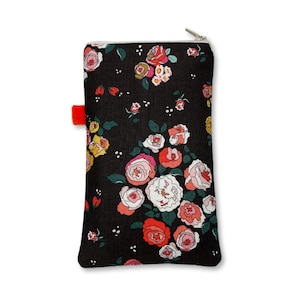 May include: A rectangular zipped pouch featuring a black fabric base with a repeating floral pattern in shades of red, pink, white, and yellow. The pouch includes a small, bright orange fabric tab protruding from the left side near the top.
