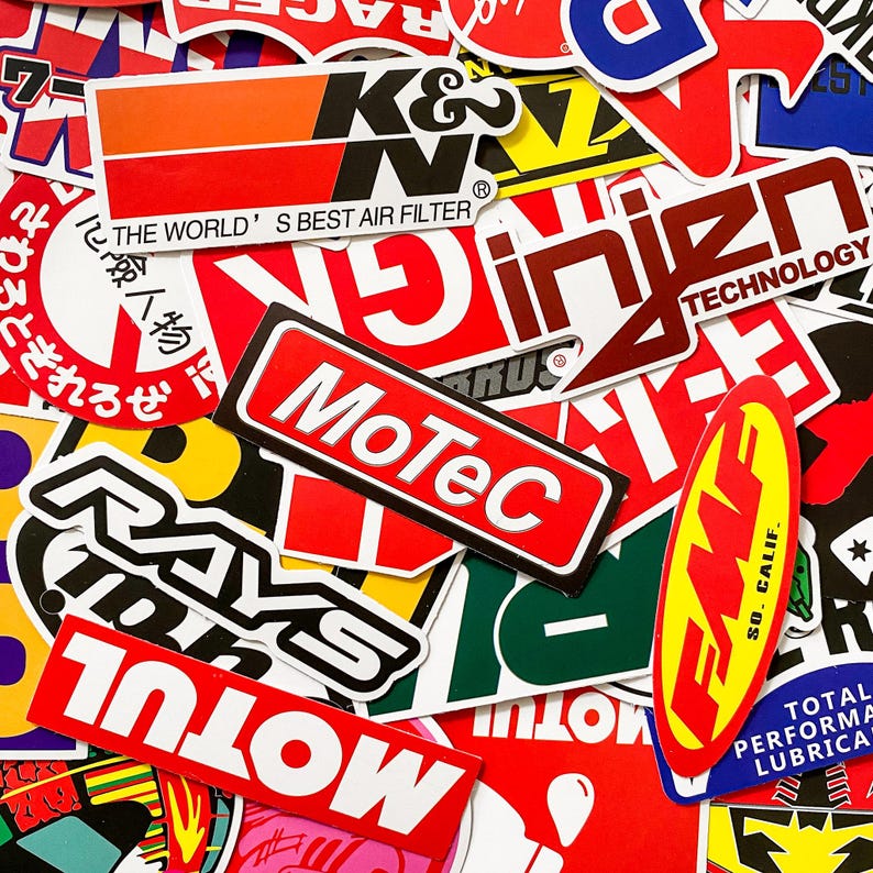 Pode incluir: Uma cole&ccedil;&atilde;o de autocolantes coloridos com v&aacute;rios log&oacute;tipos e texto. Os autocolantes apresentam marcas como K&N, MoTeC e Rays, com designs em vermelho, branco, preto e amarelo. Alguns autocolantes t&ecirc;m texto japon&ecirc;s.