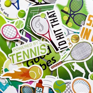 Puede incluir: Una colección de pegatinas con temática de tenis con varios diseños. Las pegatinas presentan raquetas de tenis, pelotas de tenis y frases como "Powered by Tennis" e "I'd hit that". La paleta de colores incluye verde, blanco, rojo y amarillo.