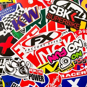 Pode incluir: Uma cole&ccedil;&atilde;o de autocolantes coloridos com v&aacute;rios designs e texto. Os autocolantes apresentam log&oacute;tipos, textos como "SBK SUPERBIKE", "FACTORY EFFEX" e "NO FUN", e elementos gr&aacute;ficos em vermelho, branco, preto e outras cores. Os autocolantes sobrep&otilde;em-se.