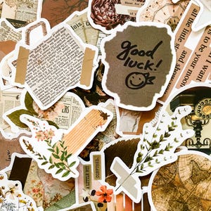 May include: A collection of vintage-style stickers and ephemera in shades of brown, beige, and green. The stickers feature botanical illustrations, newspaper clippings, and handwritten text, including "Good luck!" and a smiley face.