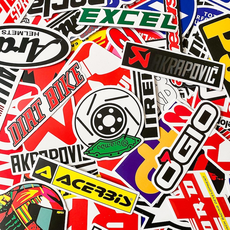 Pode incluir: Uma cole&ccedil;&atilde;o de autocolantes coloridos com v&aacute;rias marcas e log&oacute;tipos. Os autocolantes incluem "DIRT BIKE", "AKRAPOVIC", "OGIO" e "ACERBIS". A imagem &eacute; um close-up com v&aacute;rias formas e tamanhos.