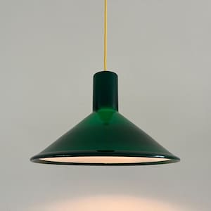 Puede incluir: Una moderna lámpara colgante verde esmeralda, con una pantalla cónica y una parte superior cilíndrica. Cuelga de un cable amarillo sobre un fondo neutro. El diseño es minimalista y elegante, adecuado para varios estilos de interiores.