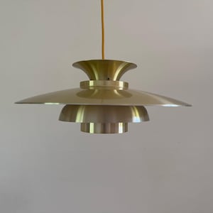 Peut inclure: Un luminaire suspendu de couleur laiton avec un abat-jour étagé en forme de soucoupe. La lumière est suspendue à un cordon fin de couleur or. Le luminaire a un design moderne du milieu du siècle.