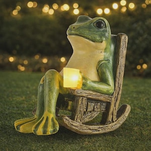 May include: A whimsical garden statue of a frog seated in a wooden rocking chair, holding a glowing candle. The frog is painted in shades of green and yellow, with a relaxed expression. The chair has a rustic, weathered appearance.