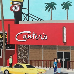 May include: A yellow vintage car parked in front of a red building with a sign that reads "Canter's" in white cursive lettering. The building also has a sign that says "Cocktails" in white lettering. There are two palm trees in the background.