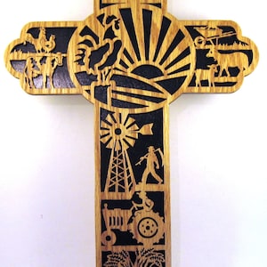 May include: A wooden cross with a black background and a farm theme. The cross features a barn, windmill, tractor, wheat, and a sunrise.