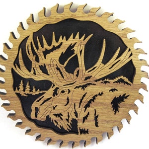 May include: A wooden saw blade with a detailed cutout of a moose head with antlers. The moose is facing the left side of the image. The background is black.
