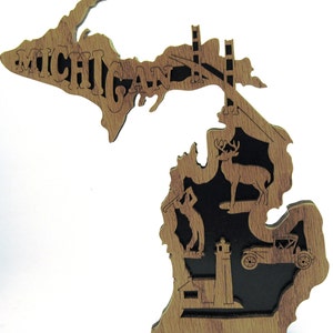 May include: Wooden cutout of the state of Michigan with the word "MICHIGAN" carved into the upper peninsula. The lower peninsula features a deer, a golfer, a lighthouse, a car, and a small house.