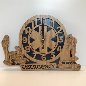 May include: A wooden clock with a black and white design featuring a medical symbol, the words "EMERGENCY", and illustrations of medical personnel and a van. The clock face has black numbers and a black hand.