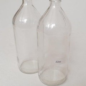 May include: Two clear glass bottles with a textured surface. The bottles are empty and have a wide mouth opening.