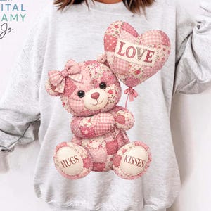以下が含まれることがあります： 「LOVE」の文字が入ったハート型の風船を持った、ピンクのパッチワークのテディベアが特徴のライトグレーのスウェットシャツ。「HUGS」と「KISSES」が足に書かれています。「DIGITAL DREAMY by Jo」の文字が左上にあります。