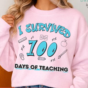 May include: A light pink sweatshirt with the text "I SURVIVED 100 DAYS OF TEACHING" in blue. The design includes school-themed graphics like an apple, pencil, and ruler. The words "digital download" are at the bottom of the image.