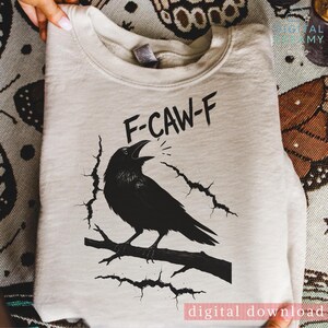 Könnte beinhalten: Cremefarbenes Sweatshirt mit einer schwarzen Grafik eines auf einem Ast sitzenden Raben, mit dem Text "F-CAW-F" darüber. Der Rabe ist mit offenem Schnabel dargestellt, und das Design enthält Risslinien. Die Worte "digital download" stehen unten.